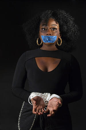 black woman with tape over her mouth and shackled