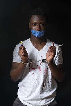 photograph of black man in t-shirt with tape over his mouth and in handcuffs