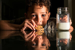 child eating a cookie with milk and reflection on table