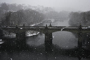 black and white photgraph of stone bridge spanning river in winter