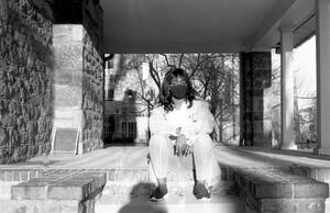 B+W photograph of woman wearing N95 mask sitting on steps outside