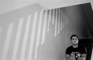 B+W photograph of main sitting on stairs and stairwell shadow