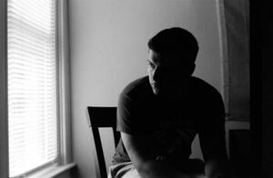 B+W photograph of man sitting at window in shadow