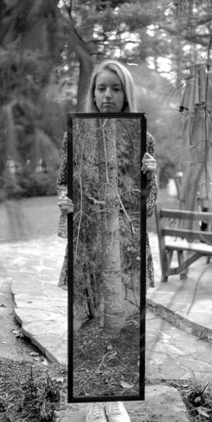B+W photograph of woman holding a large photograph of a tree in front of her