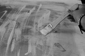 B+W photograph of paintbrush held in hand with strokes on canvas