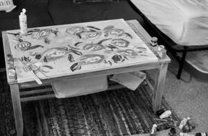 B+W photograph of partially finished canvas an paints and brushes on a table