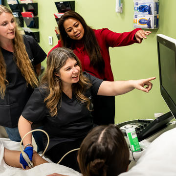 Three students working with a faculty member while using sonography equipment